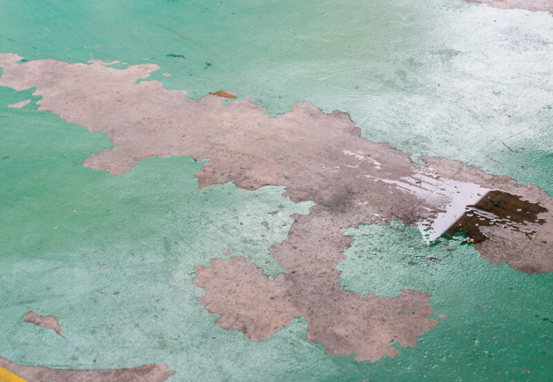 Peeling damaged epoxy layered flooring of workshop in garage from wear and tear